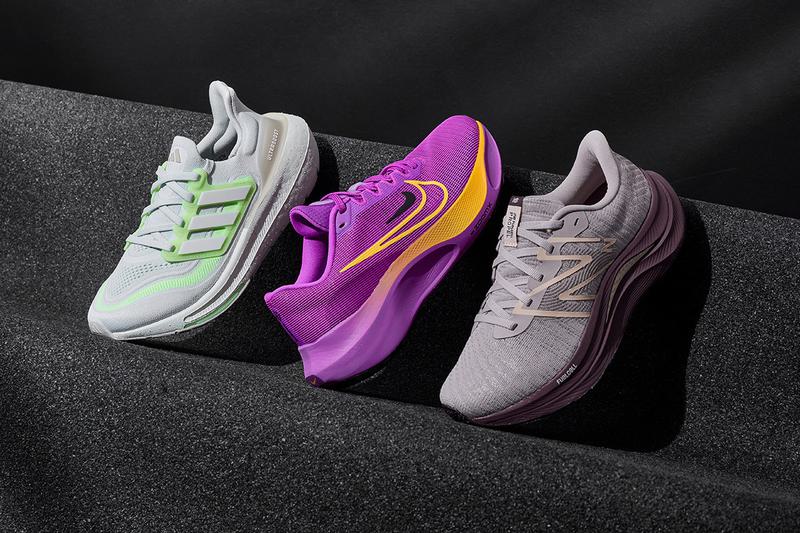 Three running shoes are displayed on a black textured surface. The first shoe is light gray with green accents, the second is bright purple with yellow and pink details, and the third is light gray with a subtle darker gray accent.