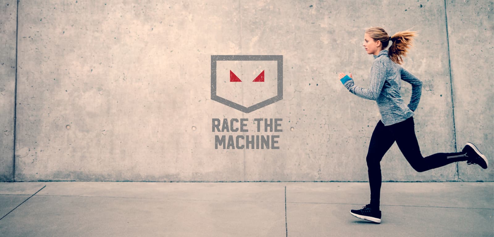 A woman wearing a gray long-sleeve shirt and black leggings is running on a concrete surface in front of a bare concrete wall. The logo "Race The Machine" with a shield and red eyes is displayed prominently in the center of the image.