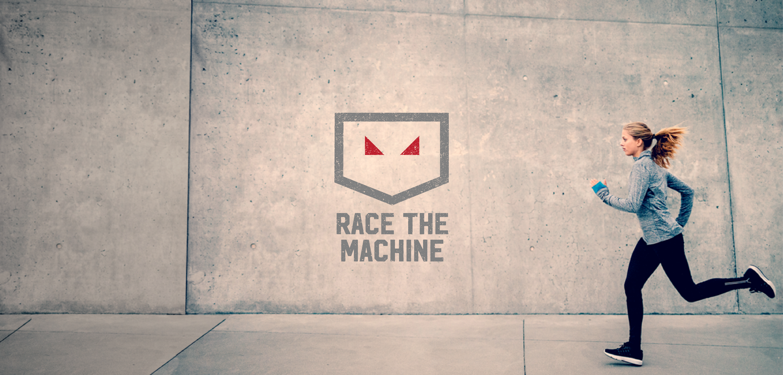 A person in athletic attire runs along a concrete wall with the "Race the Machine" logo, featuring two red triangular eyes and text beneath, prominently displayed on the wall. The individual appears focused and is holding a phone or similar device.