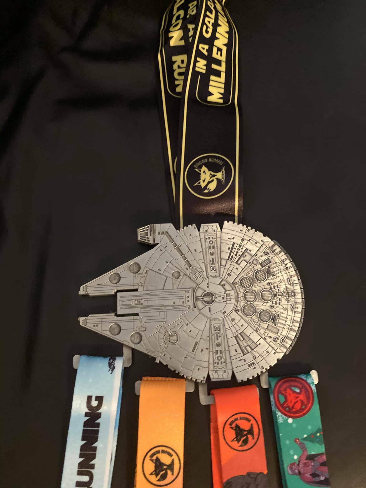 A collection of medals is displayed on a black background. The central medal features a detailed design of the Millennium Falcon from Star Wars. Attached are four colorful ribbons with different designs, all symbolizing running events.