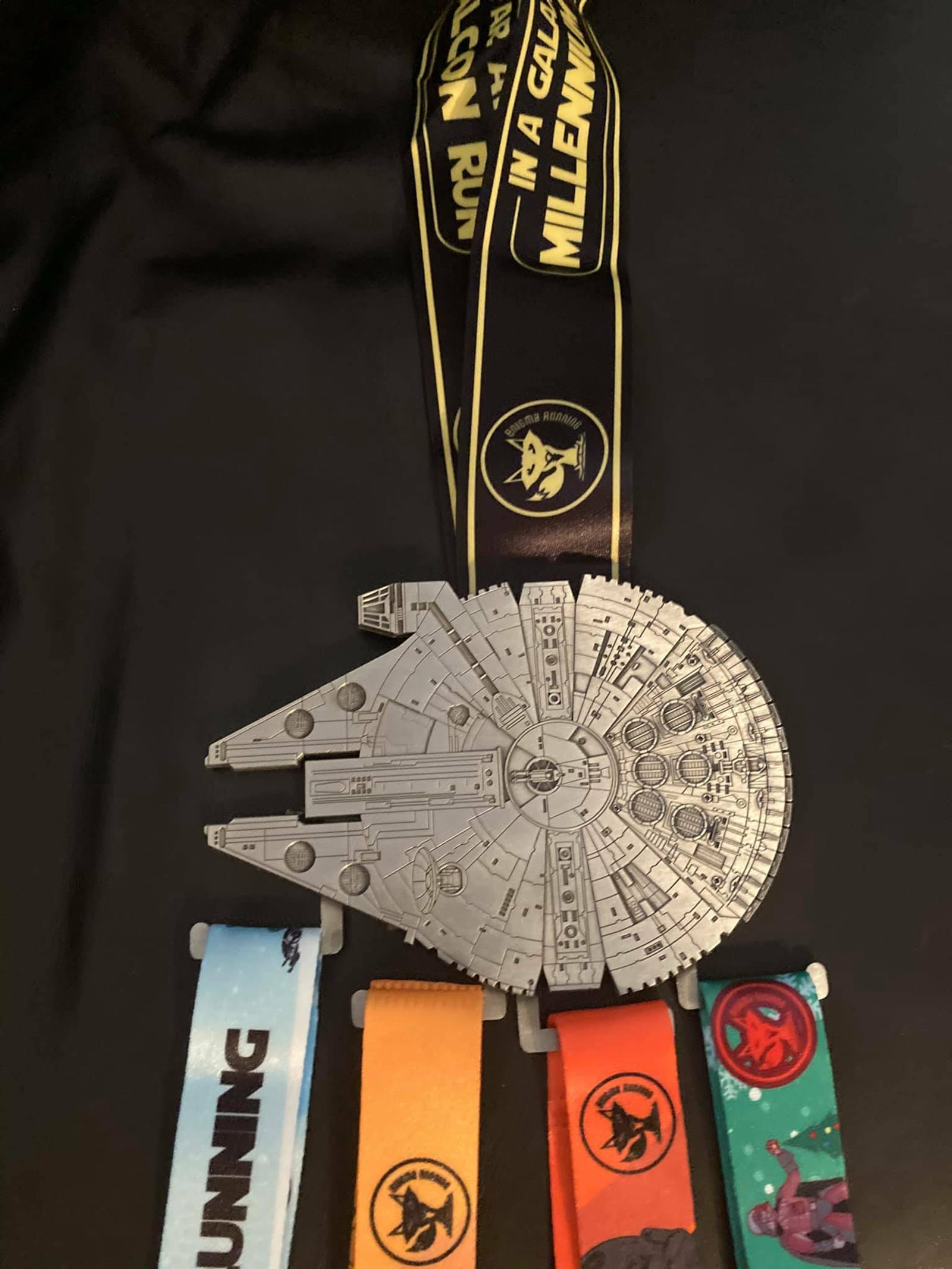 A collection of medals is displayed on a black background. The central medal features a detailed design of the Millennium Falcon from Star Wars. Attached are four colorful ribbons with different designs, all symbolizing running events.