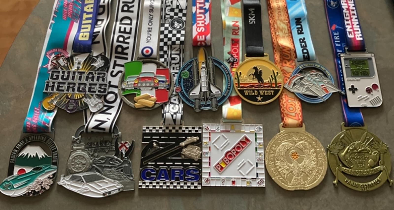 A collection of various race medals with colorful ribbons displayed on a surface. The medals feature diverse themes, including guitars, airplanes, wild west, and retro gaming, showcasing intricate designs and vibrant colors.