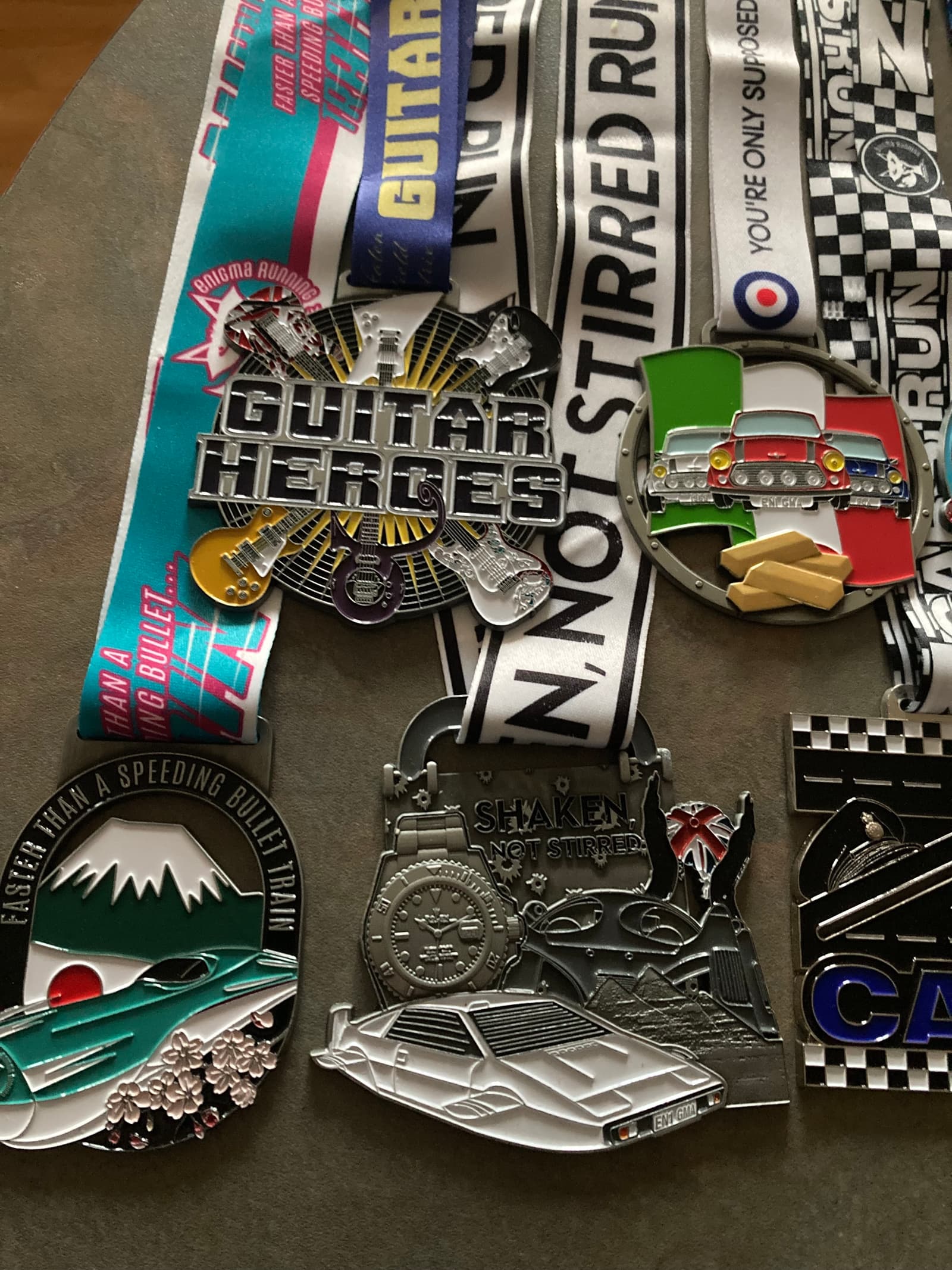 A collection of colorful marathon medals with various themes, including guitars, cars, and a landscape. Each medal has a unique design and is attached to a decorated ribbon. They are displayed on a flat surface.