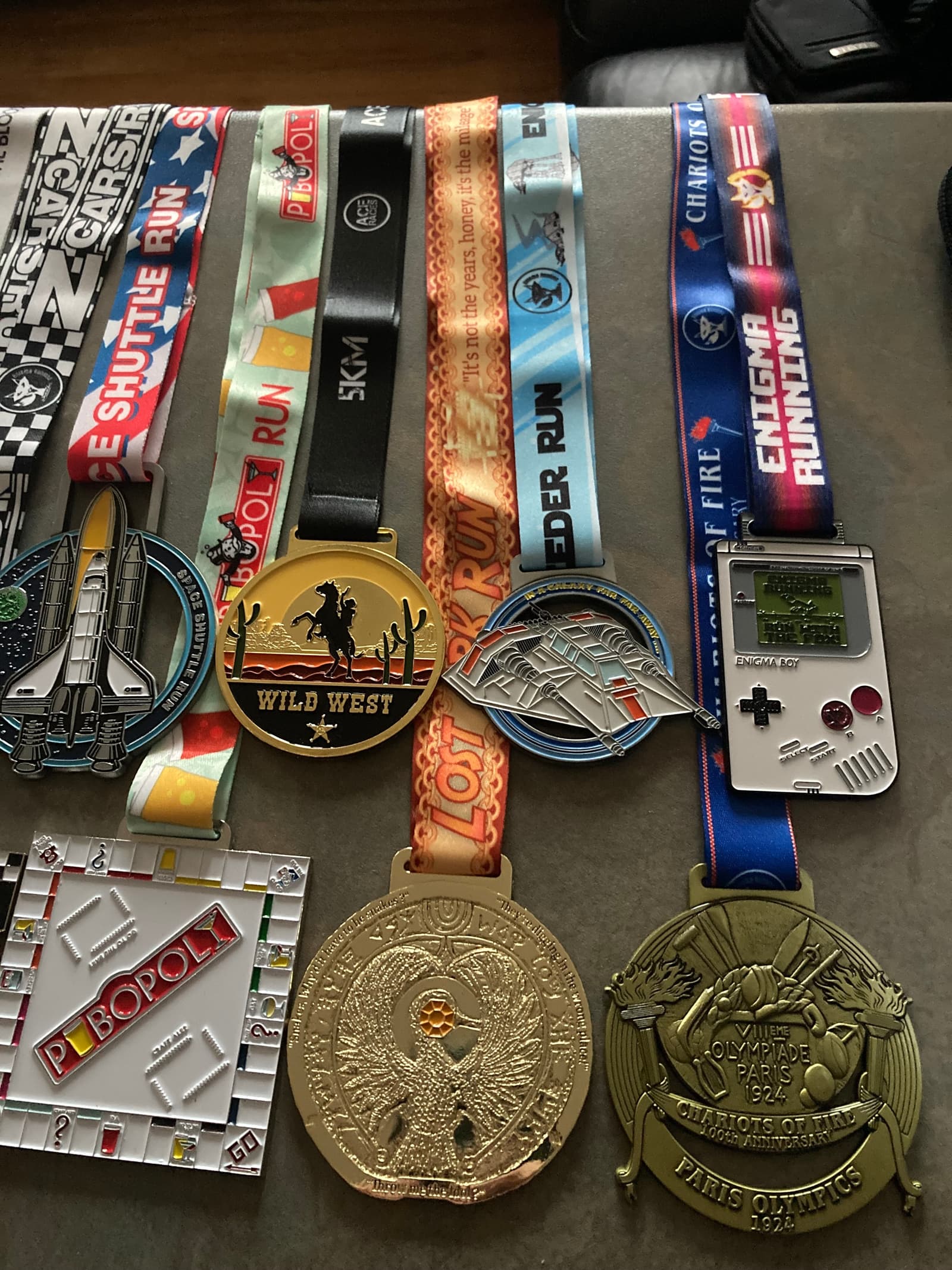 A collection of colorful medals and ribbons displayed on a table. The medals feature designs such as spaceships, a Game Boy, and various themed events. Each ribbon has distinct colors and patterns, indicating different races or achievements.