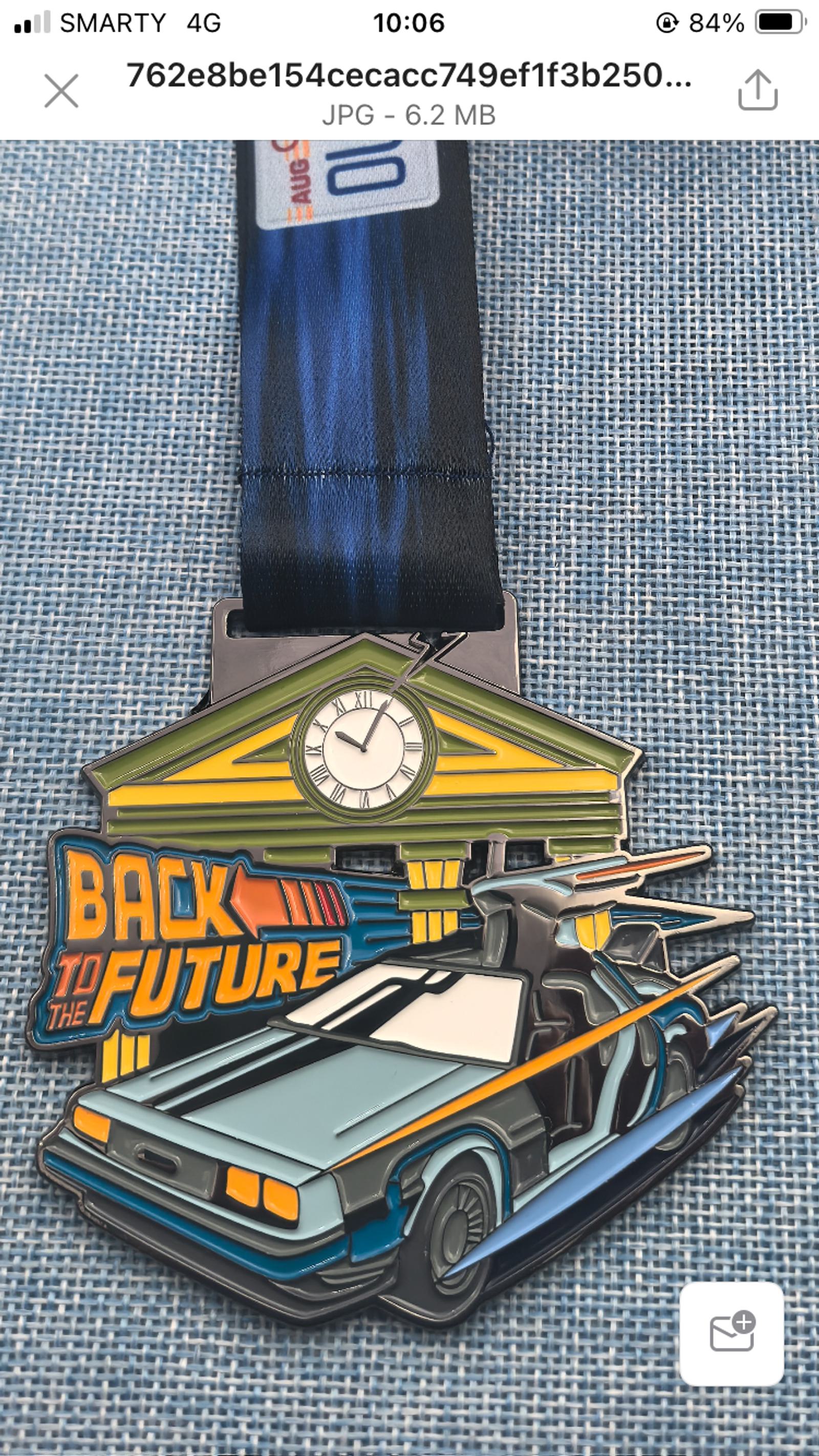 A medal featuring a stylized car with gull-wing doors in front of a clock tower, with the text "Back to the Future" in bold letters. The medal is placed on a blue textured surface.