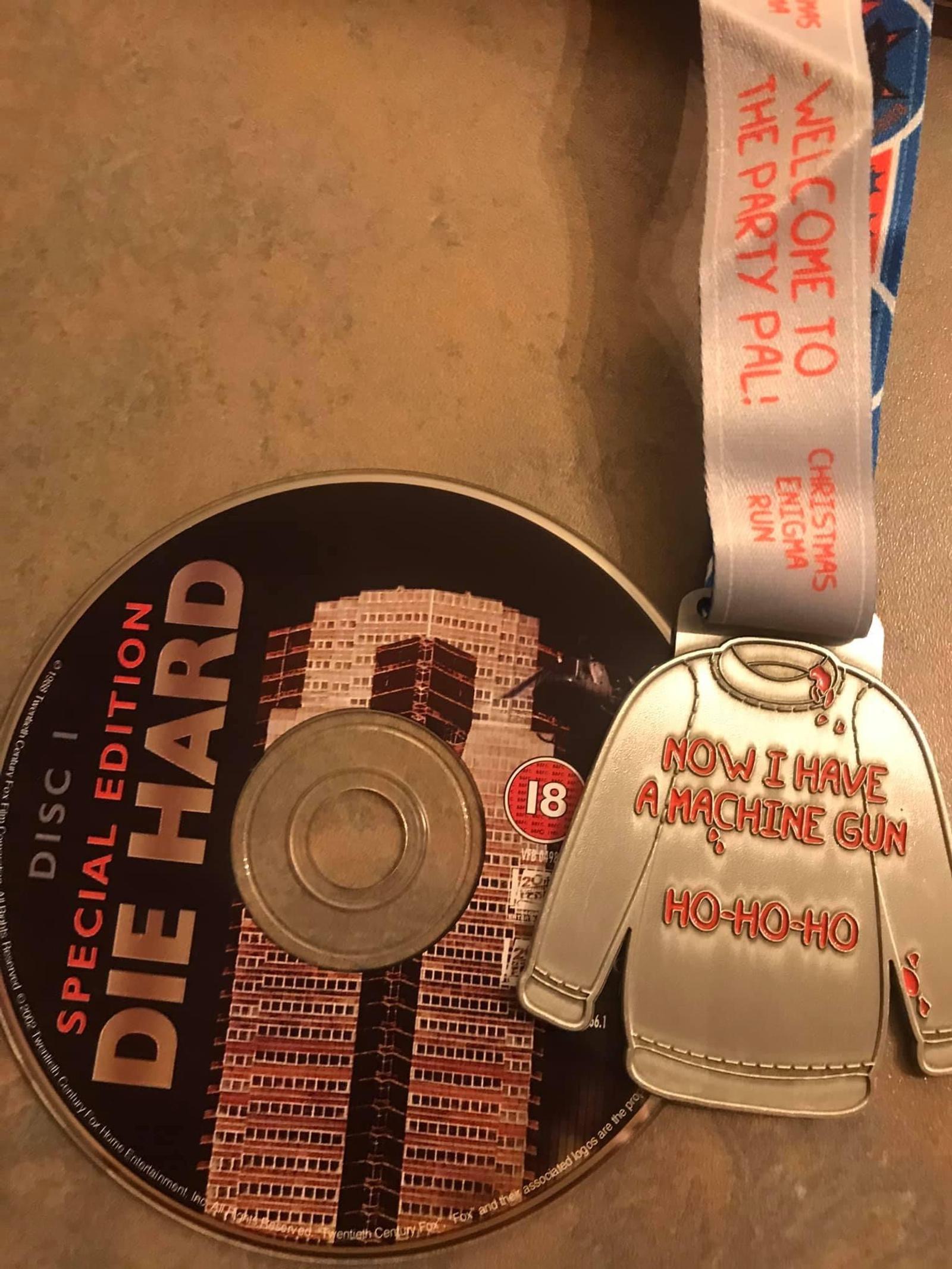 A Die Hard special edition DVD sits next to a Christmas-themed medal. The medal resembles a sweater with the text "Now I have a machine gun" and "Ho-Ho-Ho," referencing a famous quote from the movie.