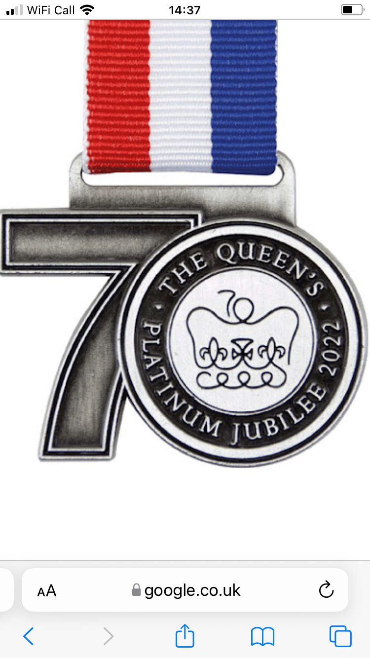 A commemorative medal featuring a large number "70" with a circular centerpiece. The center has a crown illustration and reads "THE QUEEN'S PLATINUM JUBILEE 2022." The medal's ribbon is striped in red, white, and blue.
