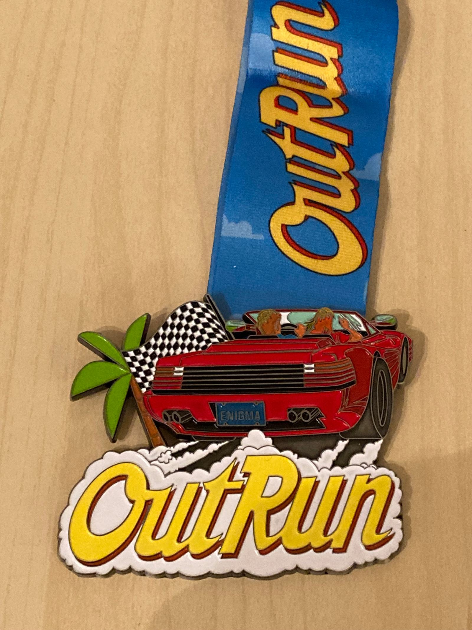 A medal featuring the text "OutRun" on a blue and yellow ribbon. The medal depicts a red sports car with two passengers driving with a checkered flag and a palm tree in the background. The word "OutRun" is prominently displayed at the bottom of the medal.