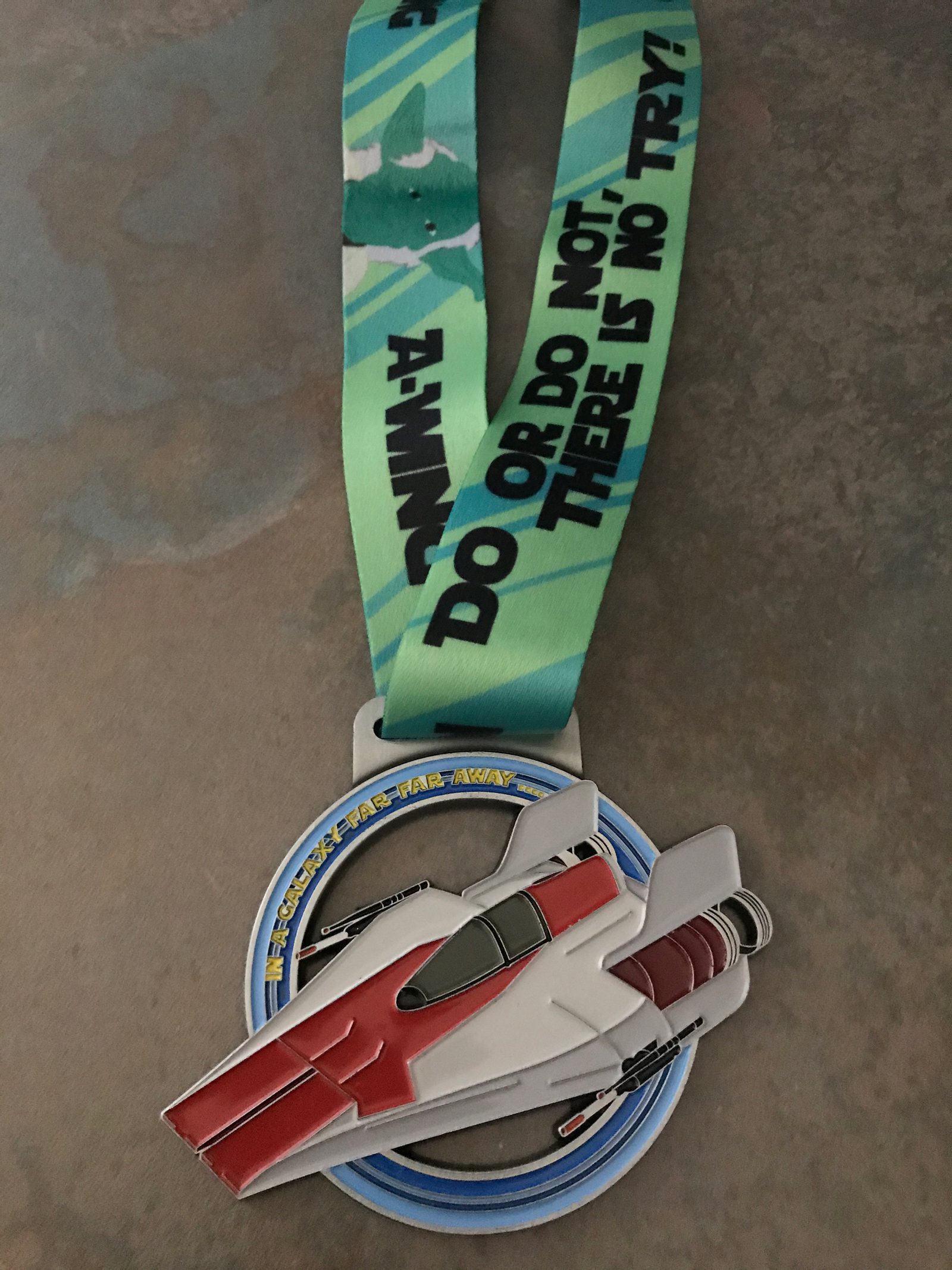 A medal with a starfighter design and an attached ribbon. The ribbon features text reading, "DO OR DO NOT. THERE IS NO TRY!" with a pattern of spacecraft and stars in the background. The medal itself is shaped like a red and white starfighter.