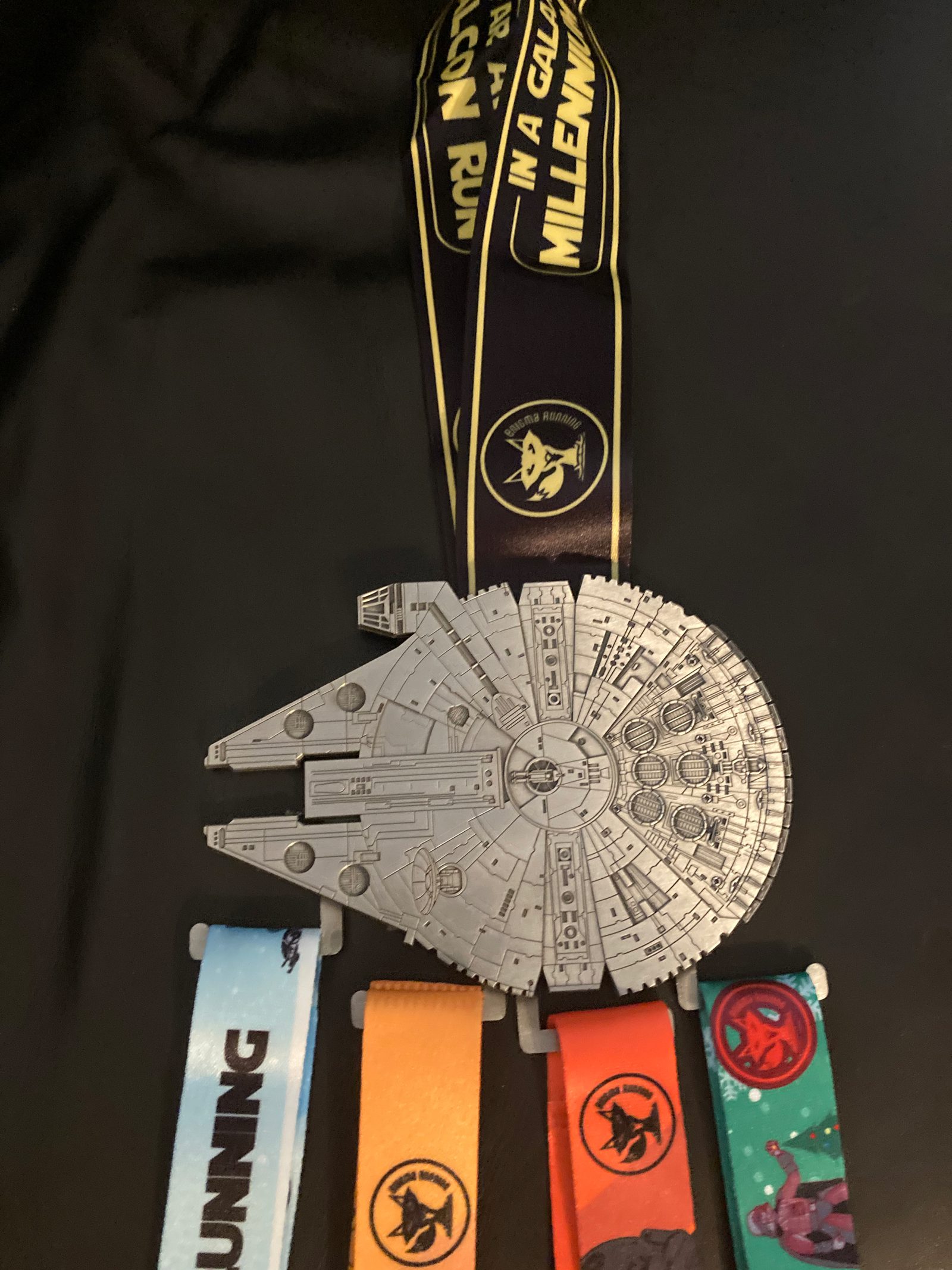 A large Millennium Falcon-shaped medal hangs from a black and yellow ribbon with the text, "IN A GALAXY FAR FAR AWAY." Four additional smaller medals with colorful ribbons, each featuring different designs, are attached at the bottom of the large medal.