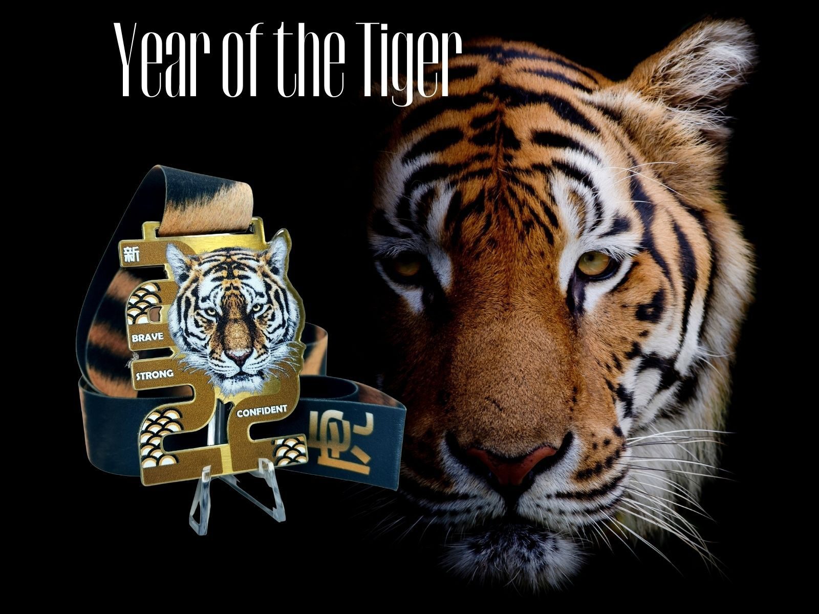 Close-up image of a tiger's face with the text "Year of the Tiger" at the top. Next to the tiger is a medal featuring a tiger illustration and the words "Brave," "Strong," and "Confident" on a ribbon. The background is black, emphasizing the tiger's intense gaze.