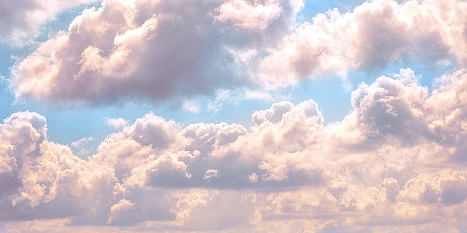 A sky filled with fluffy, white clouds illuminated by sunlight. The clouds have various shapes and sizes, with some areas showing the bright blue sky peeking through. The overall scene gives a soft, serene, and airy feel.