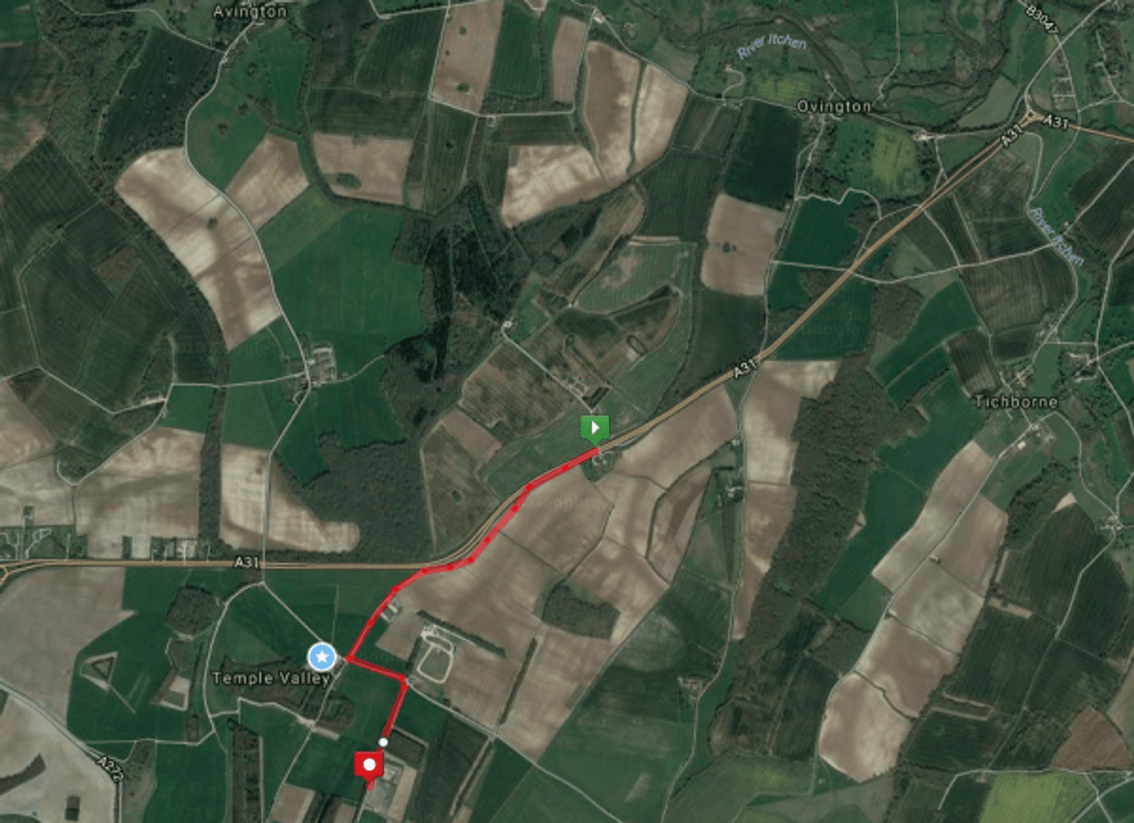 A satellite map view showing a rural landscape with fields and sparse greenery. The map is marked with red and white pins indicating locations. A red path connects the pins, traveling through fields and crossing a main road labeled A31. Nearby towns are Avington and Ovington.