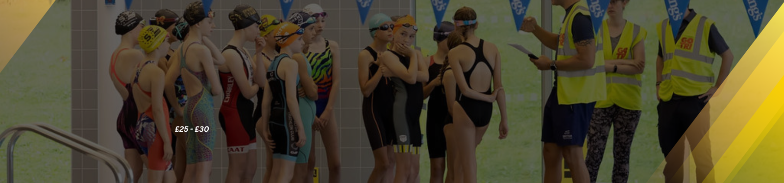 A group of young swimmers in swimsuits and caps stand by an indoor pool, listening to instructions from two adults in high-visibility vests. The pool deck has tiled flooring, and a large window provides natural light.