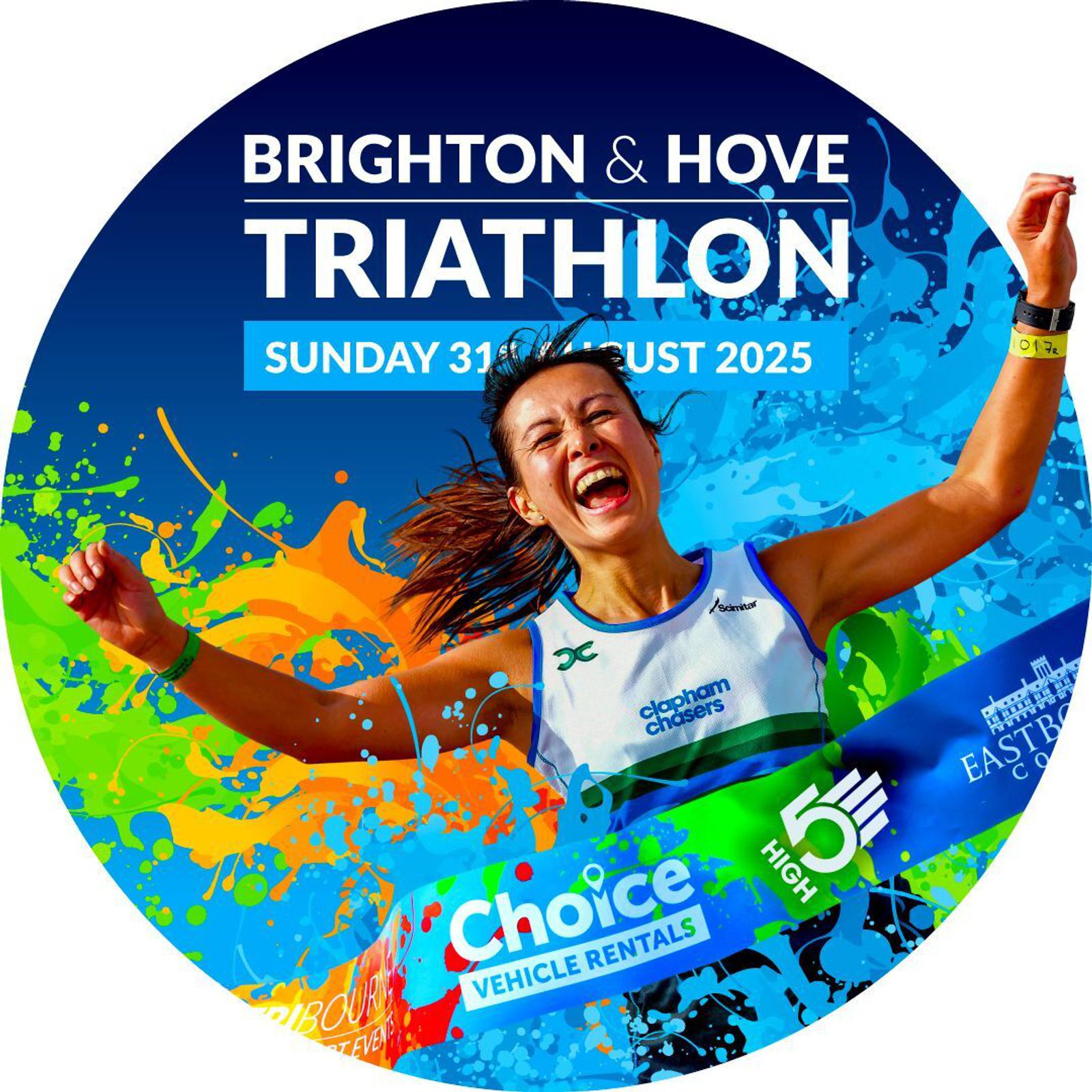 A jubilant runner crossing the finish line with arms raised in triumph at the Brighton & Hove Triathlon. The event date is Sunday, 31st August 2025. Background features vibrant splashes of color and logos of sponsors Choice Vehicle Rentals and Eastbourne College.