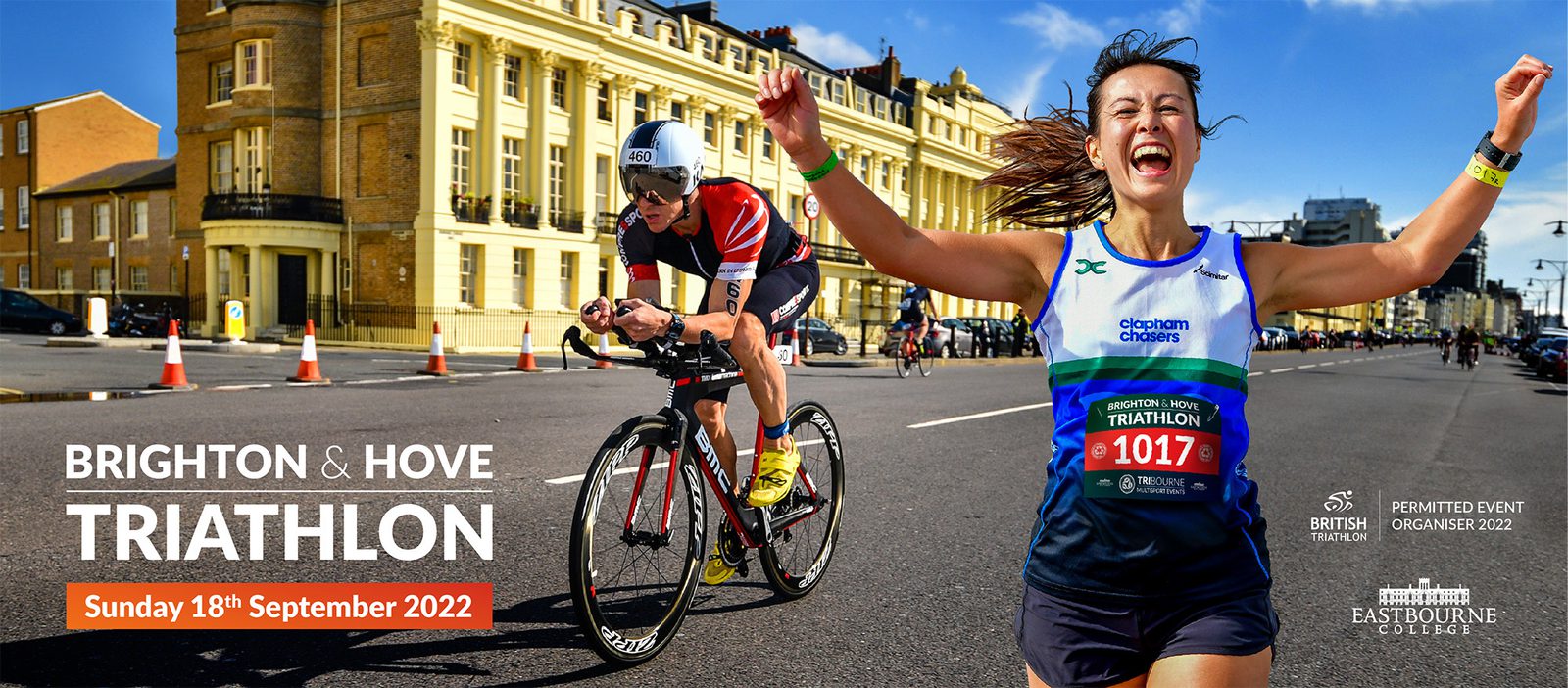 A smiling woman finishes a triathlon race with her arms raised in celebration, wearing a green and blue jersey with the number 1017. Behind her, a cyclist in a red jersey and helmet rides on a road lined with historic buildings. Text reads "Brighton & Hove Triathlon, Sunday 18th September 2022.