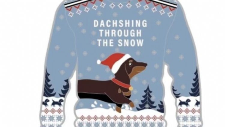 An image of a blue holiday-themed sweater featuring a dachshund dog wearing a Santa hat. The text on the sweater reads "Dachshing Through the Snow." The background includes snowflakes and trees, and the sleeves have a festive pattern.