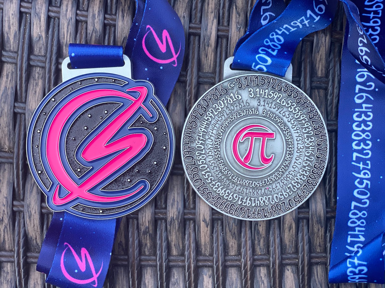 Two medals with blue ribbons are displayed on a wicker surface. The left medal features a stylized lightning bolt design, while the right medal showcases the mathematical symbol π (pi) in the center, surrounded by numerous digits of pi's value.