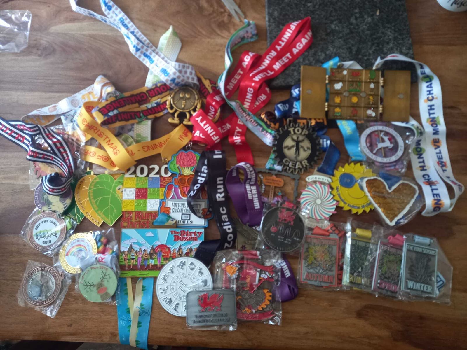 A wooden table adorned with numerous colorful medals and ribbons from various running events. The medals are of different shapes and sizes, featuring diverse designs and inscriptions that commemorate races such as marathons and themed runs.
