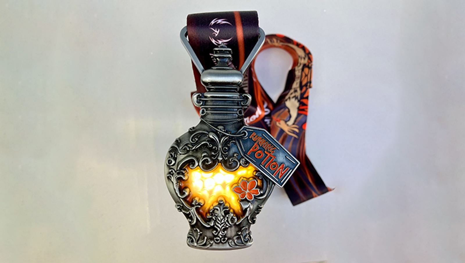 A decorative potion bottle with a glowing orange liquid inside, featuring intricate silver designs. It is attached to a dark ribbon with patterns and has a small label reading "Poison Potion.