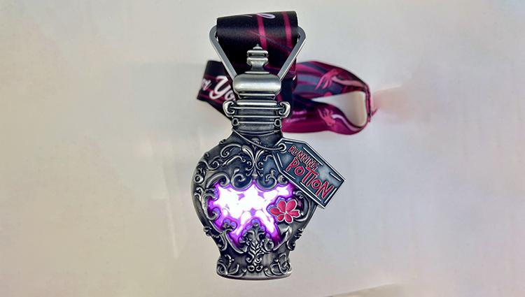 A decorative, antique-style metal bottle with intricate designs and purple light inside, attached to a ribbon. A tag reads "Running Potion." The ribbon is dark with pink accents.