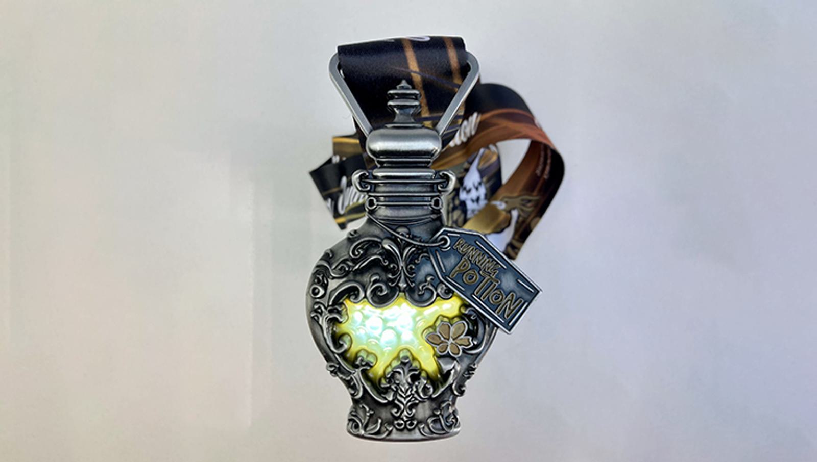 A decorative medal shaped like a potion bottle with intricate designs. It has a glowing green light inside and a label attached. The ribbon is colorful, featuring various patterns.