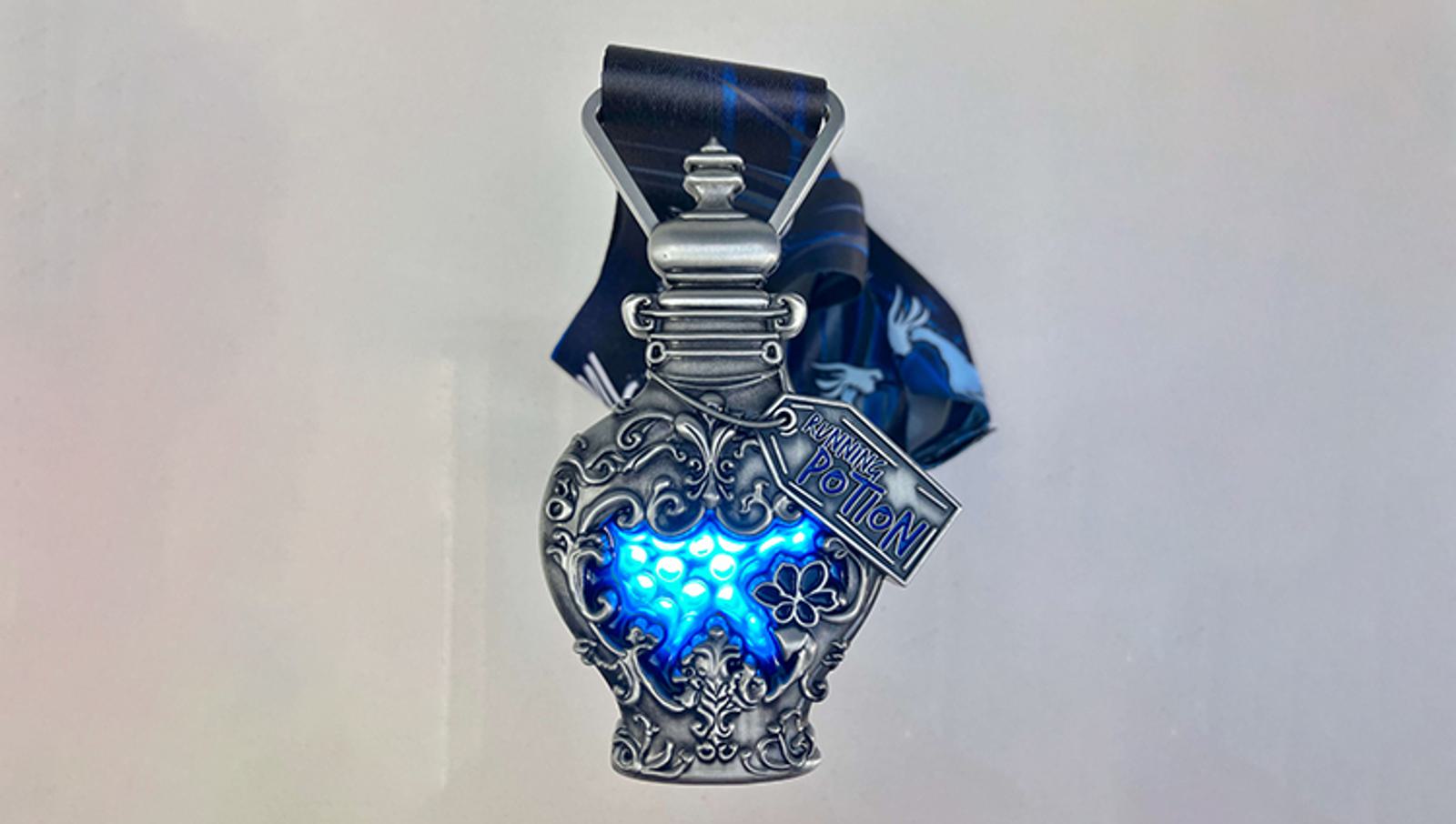 A silver, ornate potion bottle-shaped medal with blue glowing details. The bottle features decorative patterns and a small label reading "Poison Potion." It is attached to a dark blue ribbon.