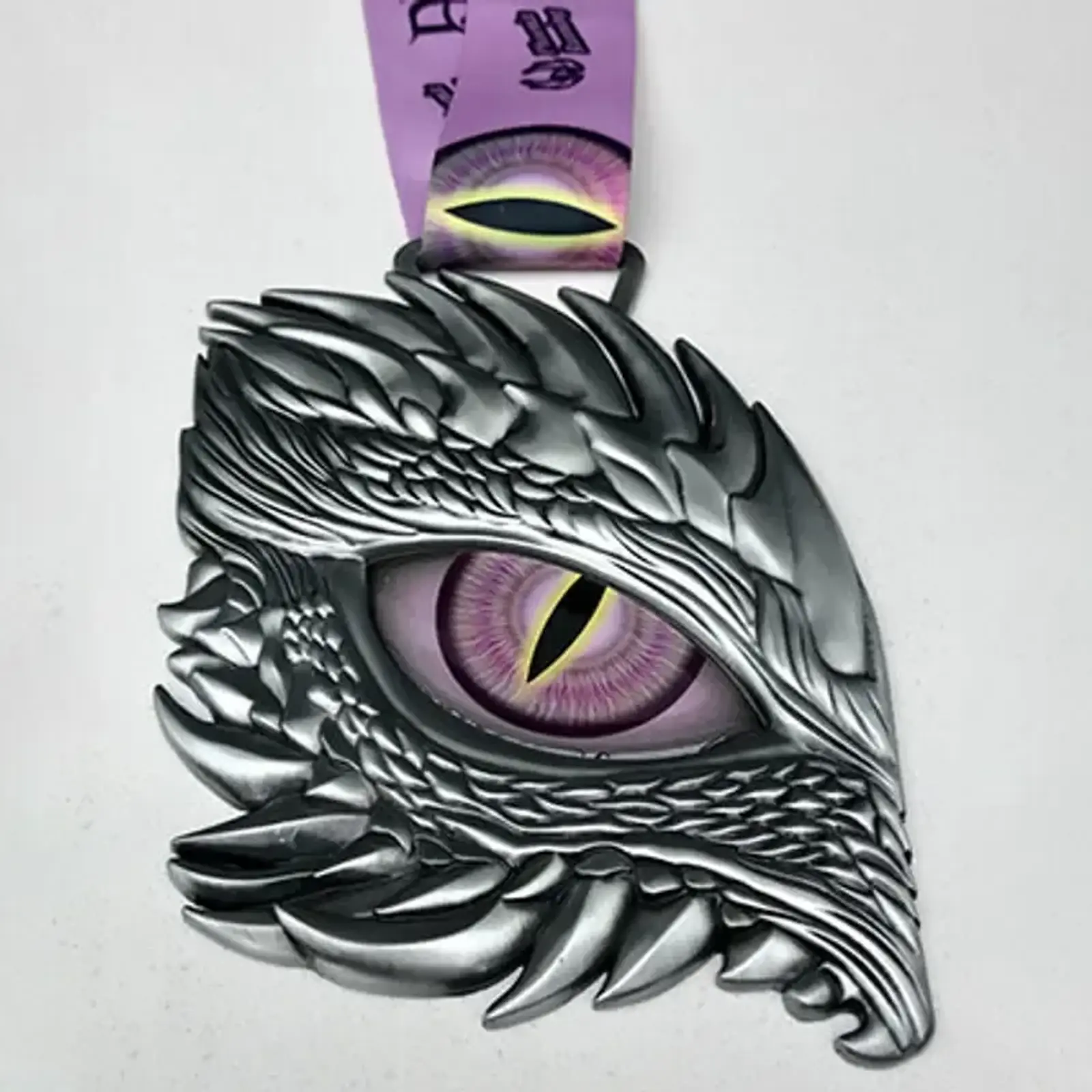 A silver dragon eye-shaped medal with intricate scale details and a purple and yellow slit pupil. It hangs from a purple ribbon with abstract designs.