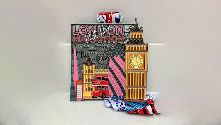 London Marathon medal featuring Big Ben, a red double-decker bus, and a telephone booth. The medal includes the London Eye silhouette and is displayed with a ribbon decorated with British flag motifs.