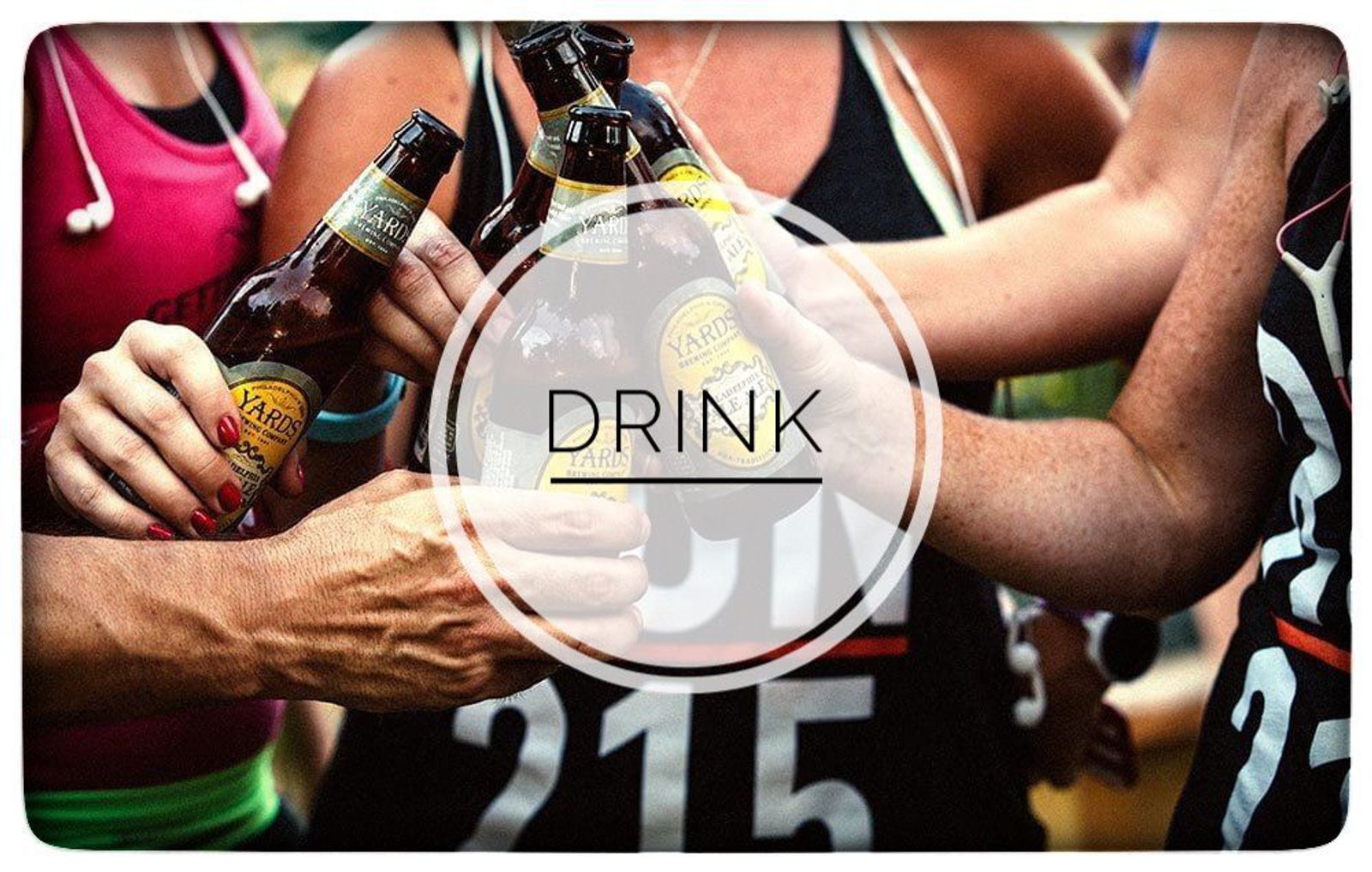 A group of people clinking beer bottles together in a celebratory manner. The word "DRINK" is prominently displayed in the center of the image. The participants are wearing race bibs with numbers, indicating they might be celebrating after a race or event.