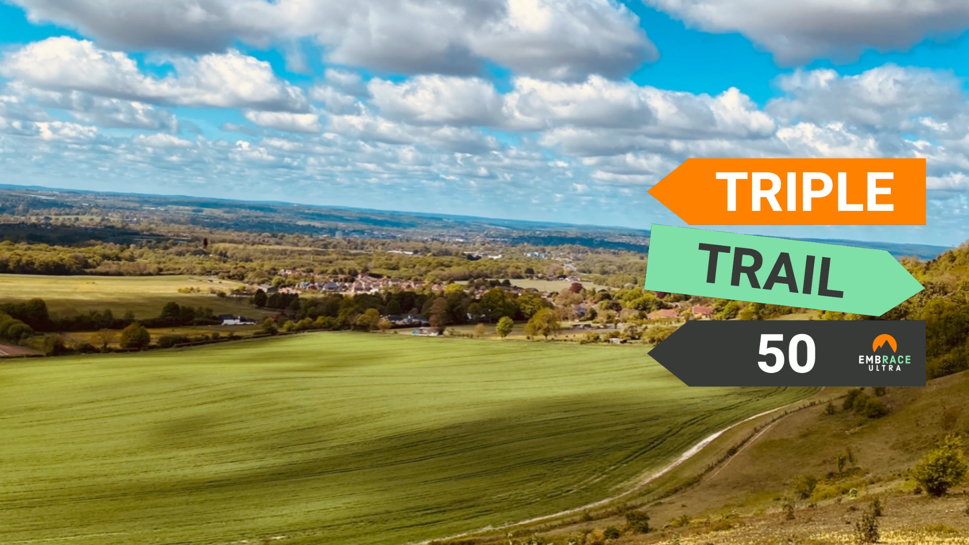 A picturesque landscape features rolling green fields, a distant village, and a blue sky with scattered clouds. Overlaying the image are colorful directional arrows labeled "TRIPLE," "TRAIL," and "50," along with an "EMBRACE ULTRA" logo on the right side.