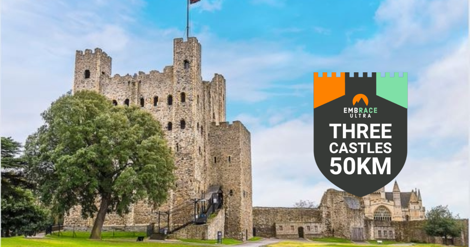 A medieval stone castle with a large central tower stands tall under a blue sky. A lush green tree is in the foreground. To the right, a badge reads "EMBRACE ULTRA THREE CASTLES 50KM" with a multicolored castle top design on the badge.