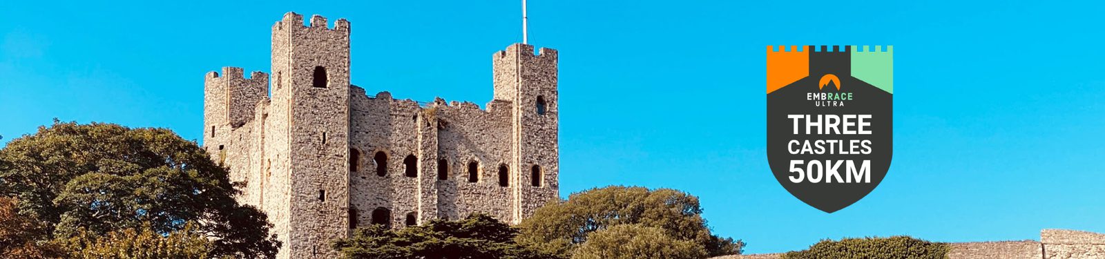 A historic stone castle with multiple towers and battlements is shown on a sunny day with clear blue skies. To the right, a shield-shaped graphic reads: "Three Castles 50KM" with the "Endure Ultra" logo above it. Trees surround the castle.