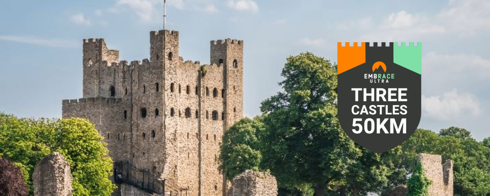 A historic stone castle with multiple towers stands amidst greenery under a blue sky. A badge on the right reads "Embrace Ultra Three Castles 50KM," suggesting an event or challenge.