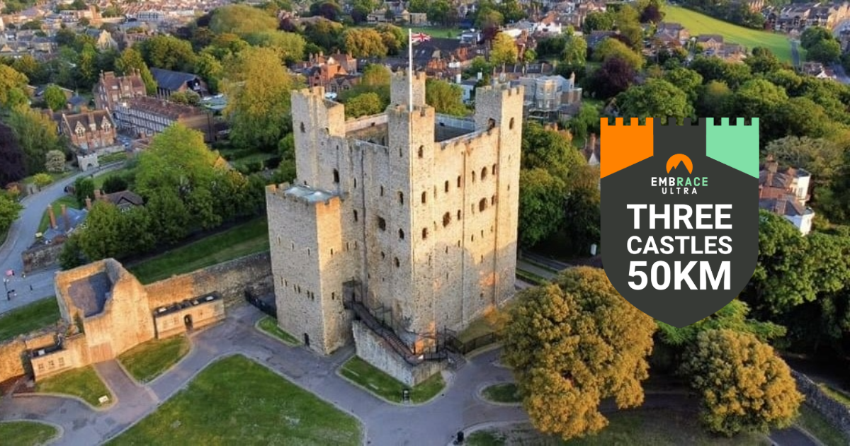 Aerial view of a historic stone castle surrounded by greenery and buildings. A logo on the right features a castle and reads "Embrace Ultra Three Castles 50KM" with orange and green accents.