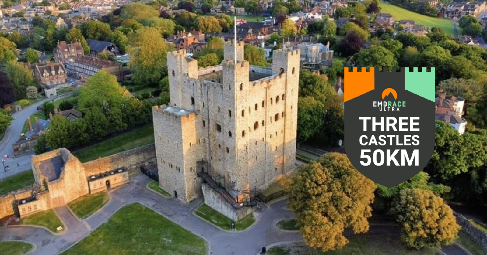 Aerial view of a historic stone castle surrounded by greenery and buildings. A logo on the right features a castle and reads "Embrace Ultra Three Castles 50KM" with orange and green accents.