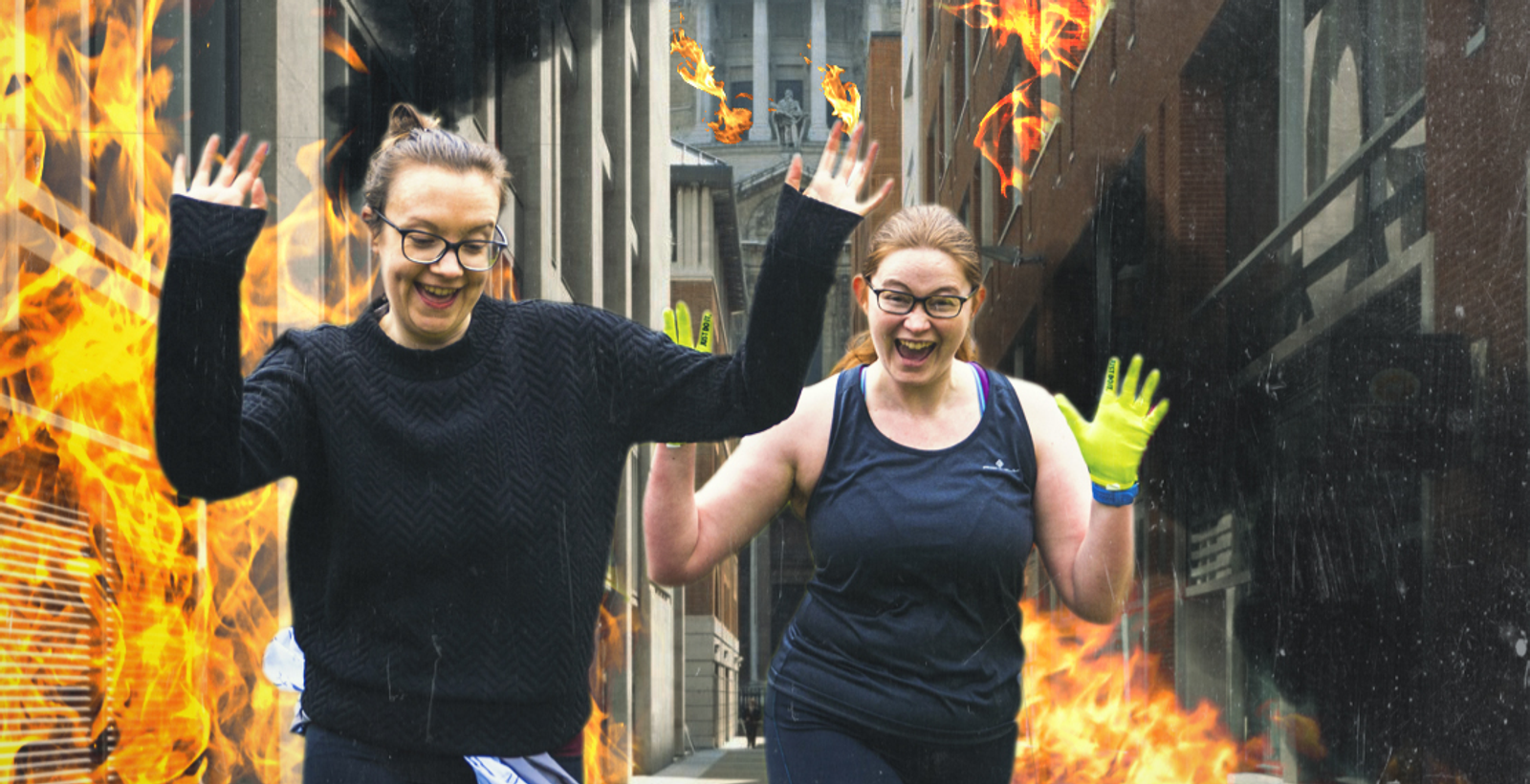 Two women with glasses joyfully run through a narrow urban alleyway flanked by walls of animated fire, with both holding their hands up in excitement. One woman wears a black sweater, and the other wears a black tank top and fluorescent yellow gloves.