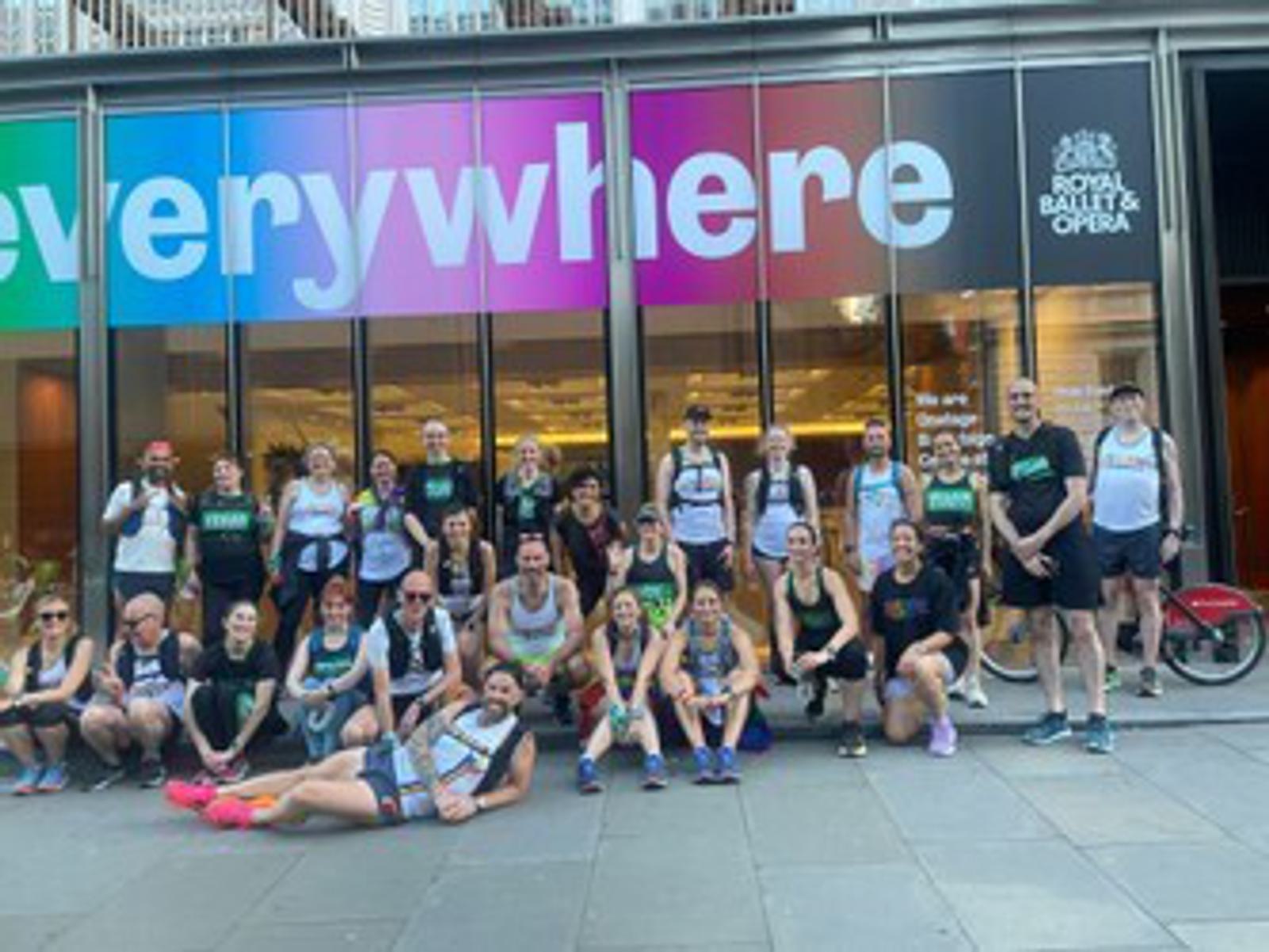 A group of people in athletic wear pose for a photo in front of a building with colorful signage that reads "everywhere." They are smiling and appear to be part of a running or fitness event.