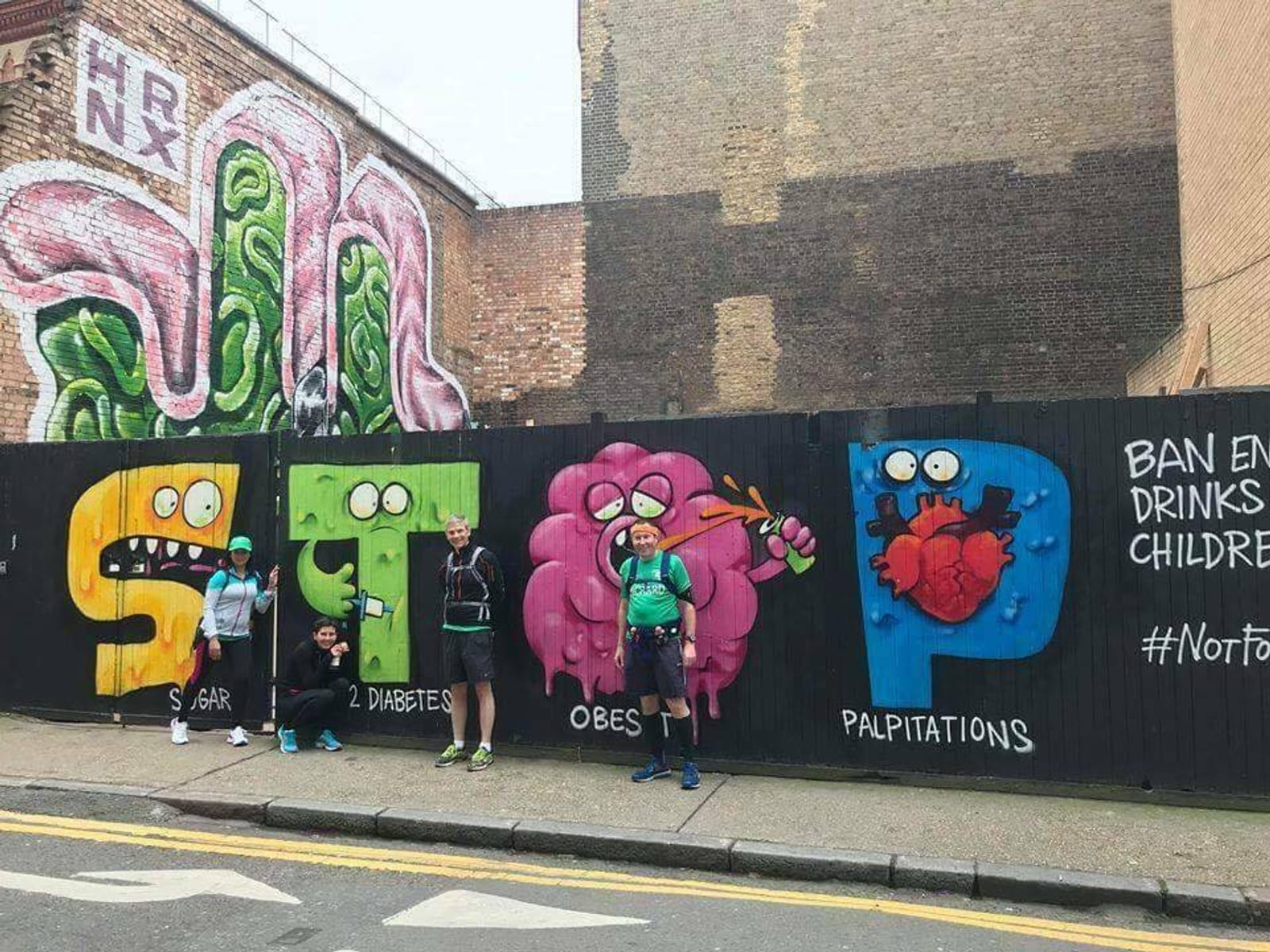 Five people in athletic wear stand in front of a large mural. The mural spells out "STOP" with each letter depicting a health issue: "S" for sugar, "T" for type 2 diabetes, "O" for obesity, and "P" for palpitations. Text demands a ban on energy drinks for children.