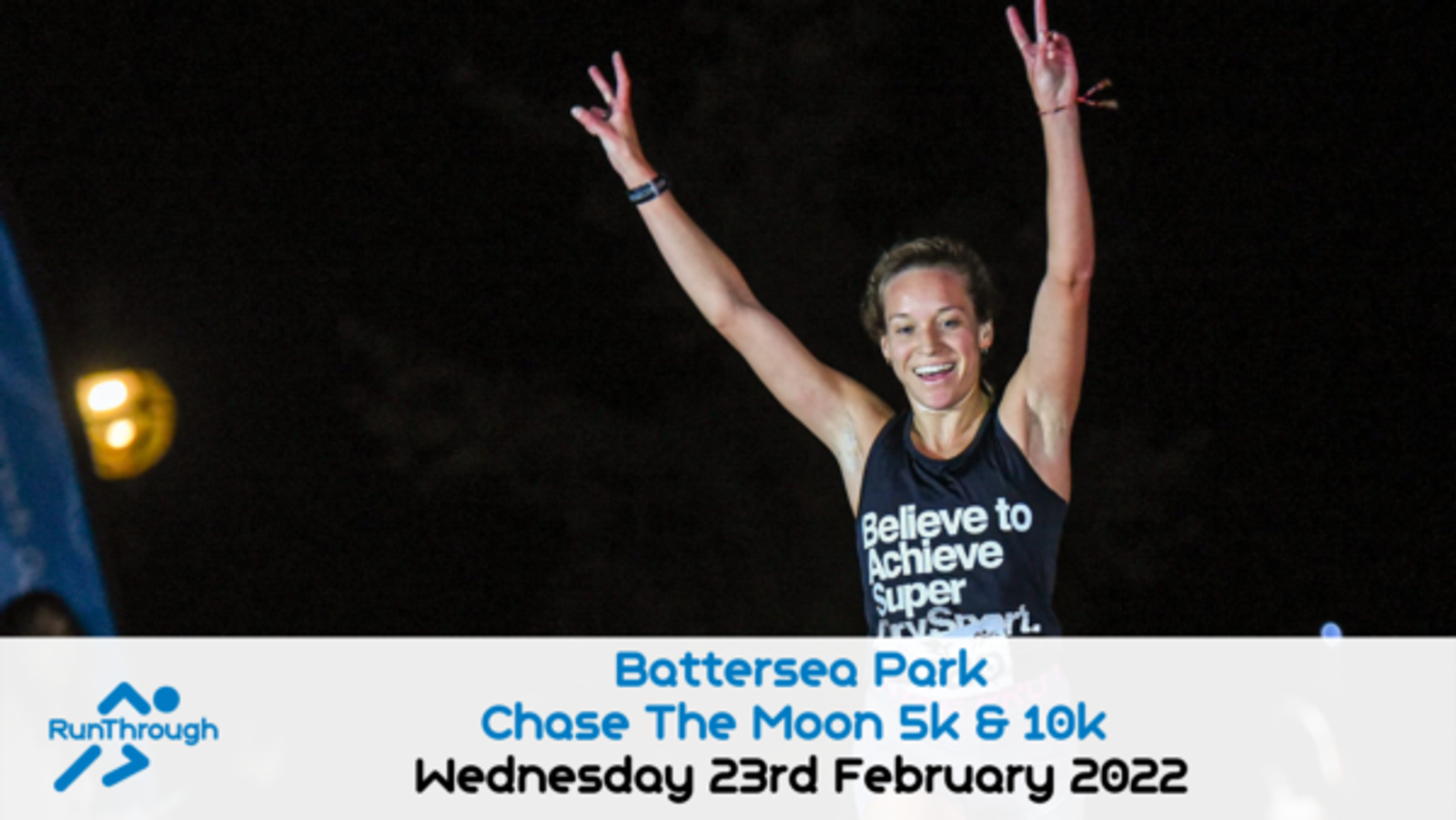A woman raises her arms in celebration after completing a race at night. She is wearing a RunThrough tank top with the text "Believe to Achieve Super Nova" on it. The event is the "Battersea Park Chase The Moon 5k & 10k" on Wednesday, 23rd February 2022.