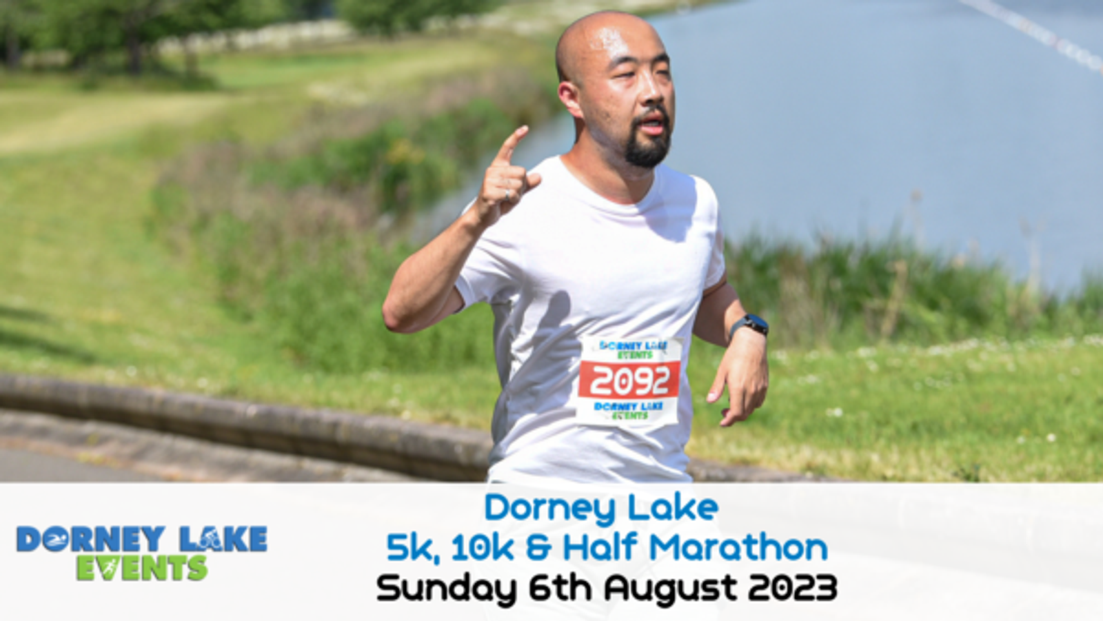 A man runs alongside a lake on a sunny day, wearing a white t-shirt and a race number bib 2092. The image promotes the "Dorney Lake 5k, 10k & Half Marathon" held on Sunday, 6th August 2023. "Dorney Lake Events" logo is displayed in the bottom left corner.