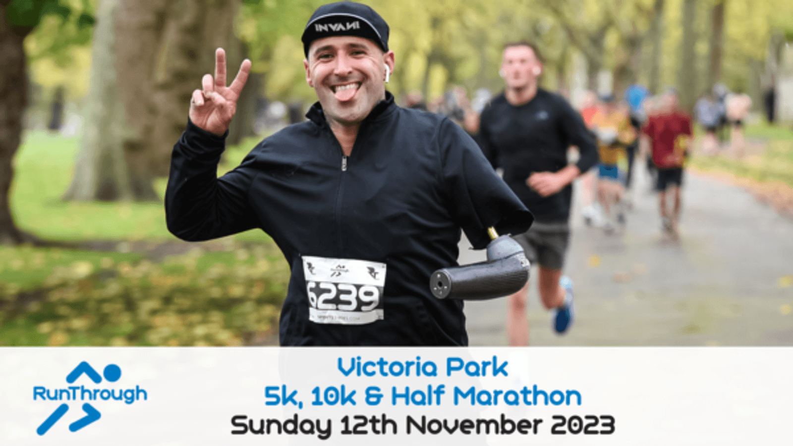 A man with a prosthetic arm is seen smiling and running in a park. He is wearing a black cap and athletic wear, with a race number "6239" pinned to his shirt. "Victoria Park 5k, 10k & Half Marathon, Sunday 12th November 2023" text is overlayed at the bottom.