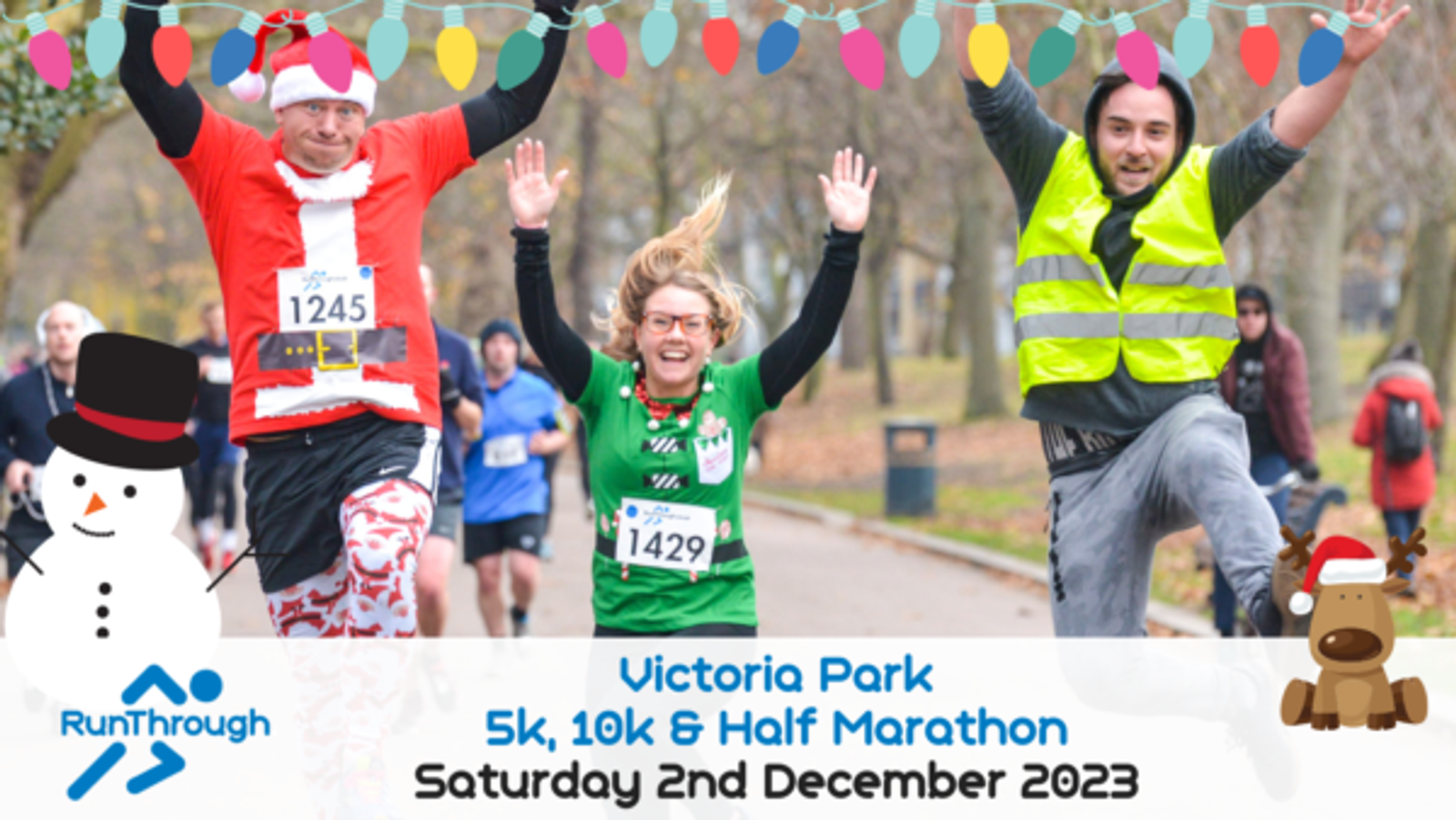 Three joyful runners, one dressed as Santa, one in a green festive shirt, and another in a safety vest, leap into the air with arms raised at Victoria Park. Decorated with colorful lights and holiday graphics, the banner announces the RunThrough event on December 2nd, 2023.