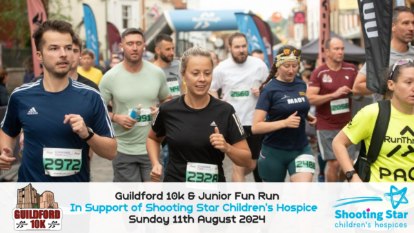 A group of runners participating in the Guildford 10k & Junior Fun Run on a city street, supporting the Shooting Star Children's Hospice. The event date is Sunday, August 11th, 2024. Runners wear race bibs, and various banners and signs are visible in the background.