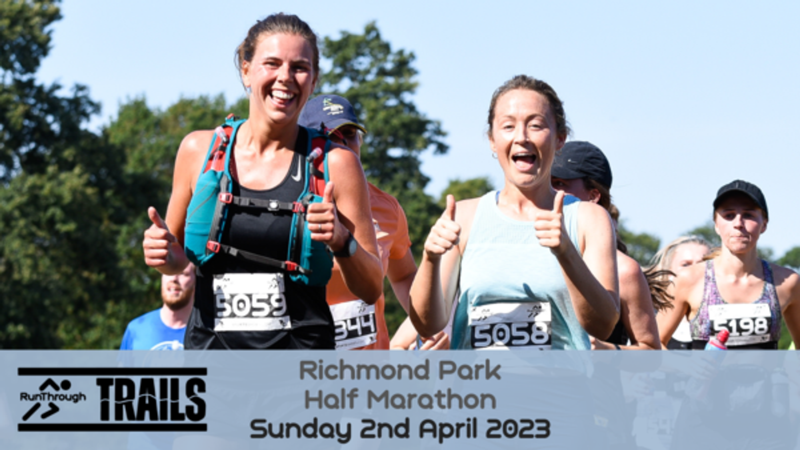A group of marathon runners, including two women in the foreground smiling and giving thumbs up, participate in the Richmond Park Half Marathon on Sunday, 2nd April 2023, organized by RunThrough Trails. The runners wear race bibs among a sunny outdoor backdrop.