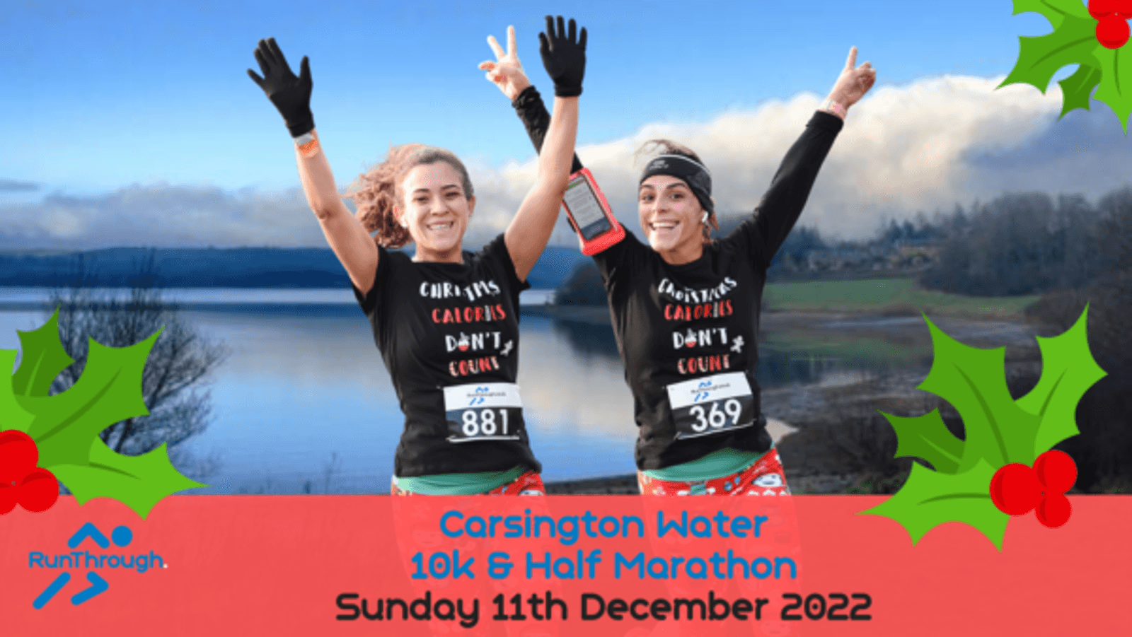 Two women smile and wave their arms in the air after completing a race. They wear matching black holiday-themed long-sleeve shirts with "Christmas Calories Don't Count" text. A scenic lake and hills are in the background. Text reads "Carsington Water 10k & Half Marathon Sunday 11th December 2022.