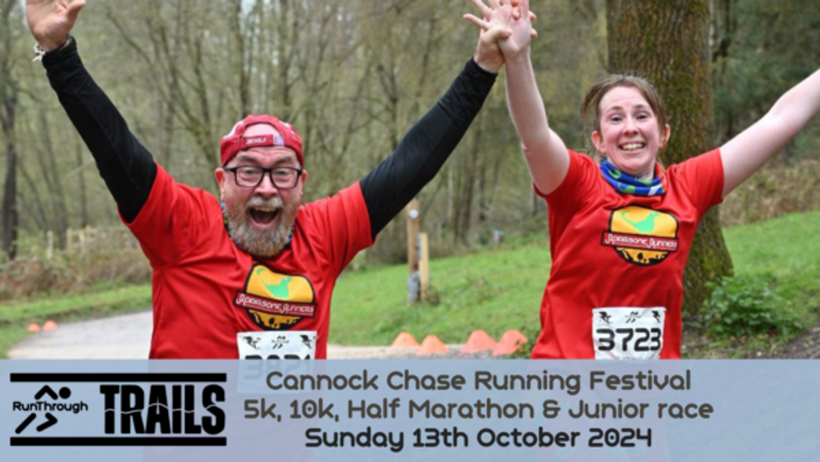 Two happy runners in red shirts raise their arms joyfully as they finish a race. Both wear race bibs, one numbered 3723. A banner below reads "Cannock Chase Running Festival 5k, 10k, Half Marathon & Junior race Sunday 13th October 2024.