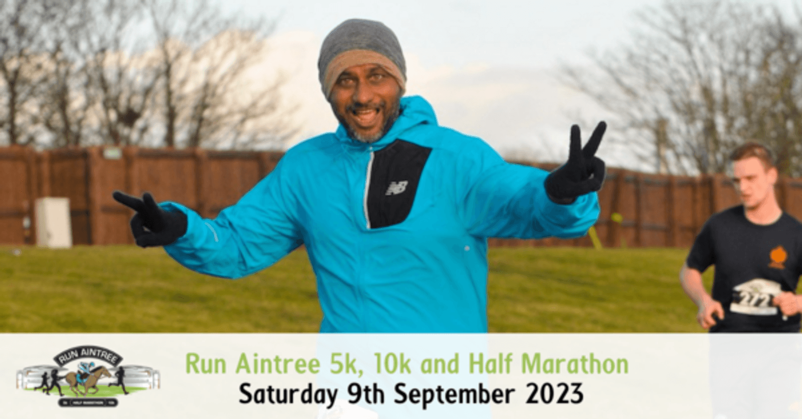 A runner in a blue jacket and gray hat poses with outstretched arms and a joyful expression during the Run Aintree event. Another participant runs in the background. Text at the bottom notes the event: "Run Aintree 5k, 10k and Half Marathon, Saturday 9th September 2023.