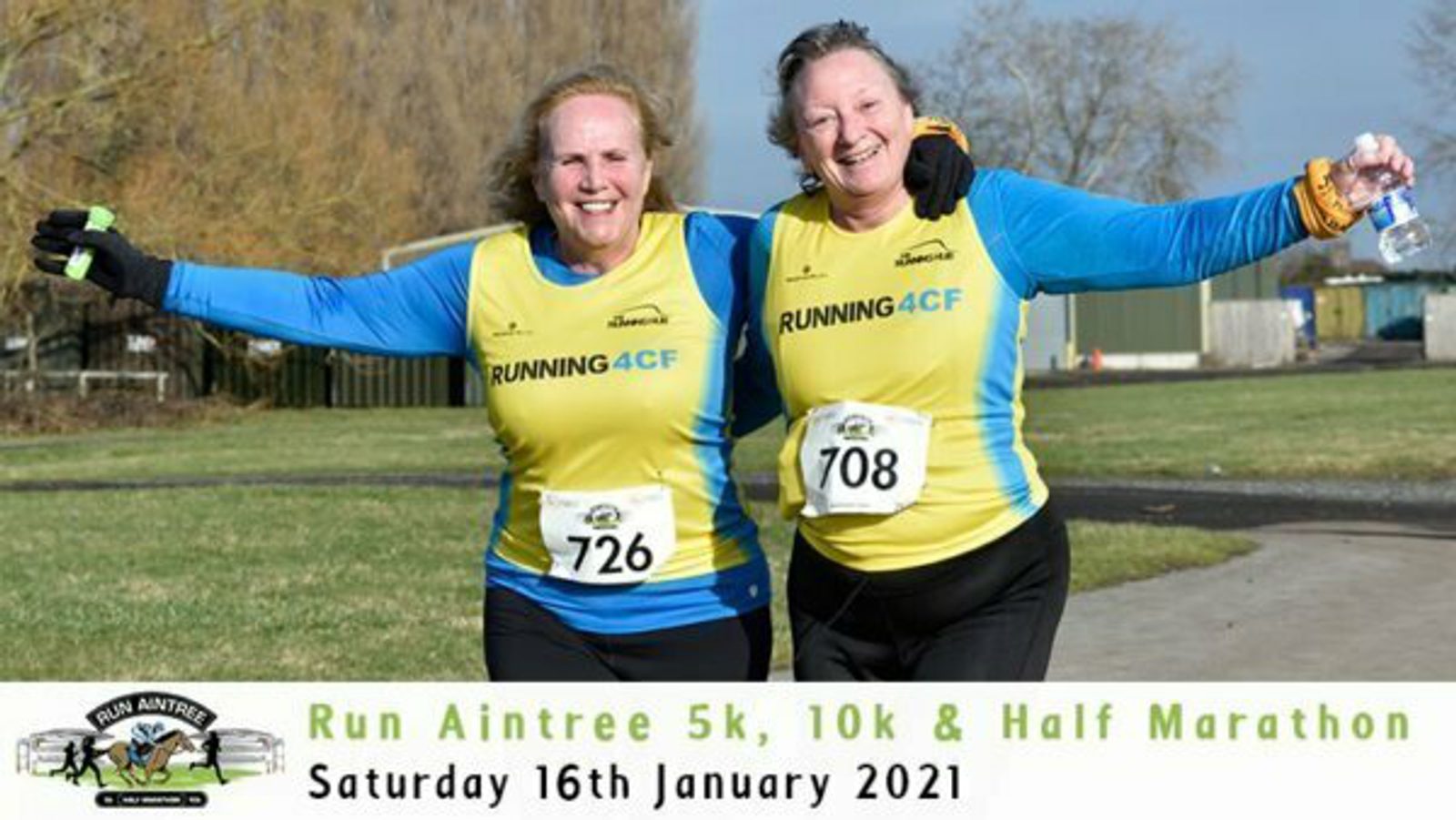 Two women in matching blue and yellow "Run Aintree" jerseys, one numbered 726 and the other 708, celebrate together with arms raised, after finishing a race. The banner on the image reads "Run Aintree 5k, 10k & Half Marathon - Saturday 16th January 2021.