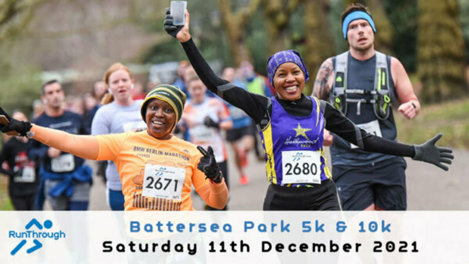 Two runners, wearing race bibs 2671 and 2680, smile and raise their hands triumphantly while running. Other participants are visible behind them. The text overlay reads, "Battersea Park 5k & 10k, Saturday 11th December 2021," with the RunThrough logo on the bottom left.